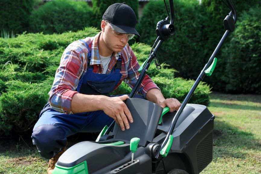Cleaning lawn mower. Young man detaching grass catcher from lawn mower